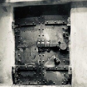 a silver & black photo of a metal bunker door with bulky lock