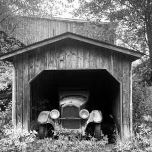 a black & white photo of a century old car peaking out of a stand alone wooden